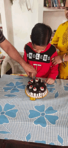 a boy wearing a endless shirt is cutting a cake