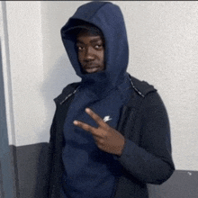 a man wearing a hooded jacket and a blue sweatshirt giving a peace sign