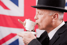 a man wearing a bowler hat is drinking from a cup in front of a british flag