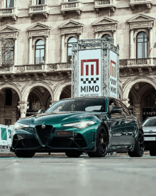 a green car is parked in front of a building with a mimo sign on it