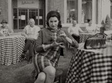 a black and white photo of a woman sitting at a table in front of a building that says wheatsmith 's