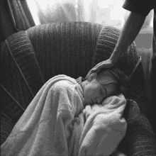 a black and white photo of a woman sleeping in a chair with her hand on her head .