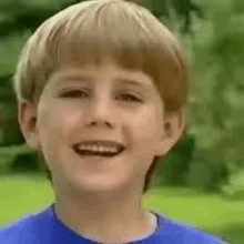 a young boy in a blue shirt is smiling in a park .