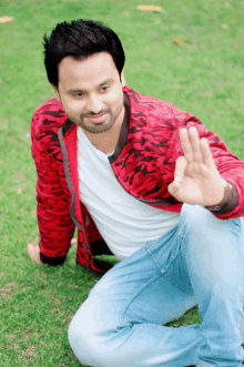 a man wearing a red jacket and a white shirt is kneeling on the grass