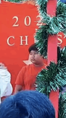 a man in a red shirt is standing in front of a christmas tree