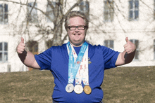 a man wearing a blue shirt with medals around his neck is giving a thumbs up