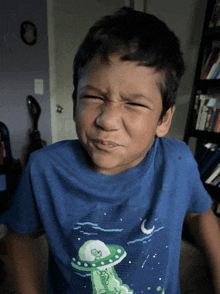 a young boy wearing a blue shirt with an alien on it making a face