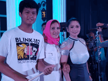 a boy wearing a shirt that says blink-182 stands next to two women