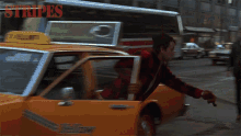 a man in a red and black plaid shirt is getting out of a yellow taxi