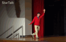 a man in a red jacket stands on a stage and waves his hand in front of a star talk logo