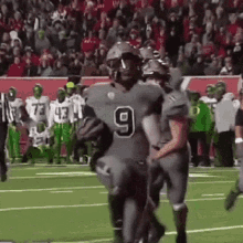 a group of football players are standing on a field . one of the players has the number 9 on his jersey .