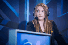 a woman wearing headphones and a black shirt with a yellow emblem on the sleeve stands in front of a computer monitor