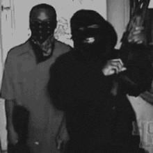 a man in a mask is holding a gun while standing next to another man .