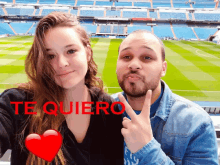 a man and a woman are posing for a picture in front of a soccer field and the words te quiero are on the bottom