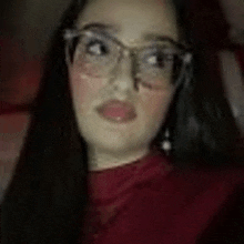 a woman wearing glasses and a red sweater is looking at the camera .