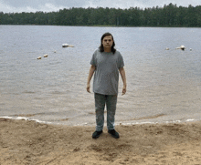 a man in a grey shirt is standing on a beach near a lake