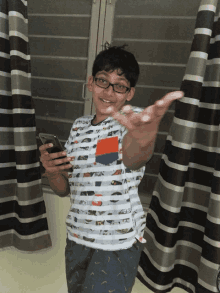 a boy wearing glasses and a striped shirt holds a cell phone in his hand