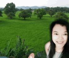 a woman is smiling in front of a green field with trees in the background