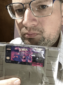 a man wearing glasses holds a super nintendo x-men game