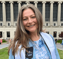 a woman in a graduation cap and gown smiles in front of a large building