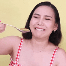 a woman in a red and white checkered top is smiling while holding a spoon in front of her face