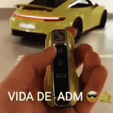 a person is holding a remote control in front of a yellow porsche 911 .