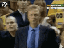 a man in a suit and tie is standing in front of a crowd watching a basketball game on nba tv