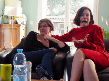 two women are sitting on a couch with a bottle of water and a can of soda