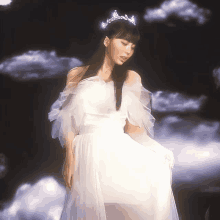 a woman in a white dress and tiara stands in front of a cloudy sky