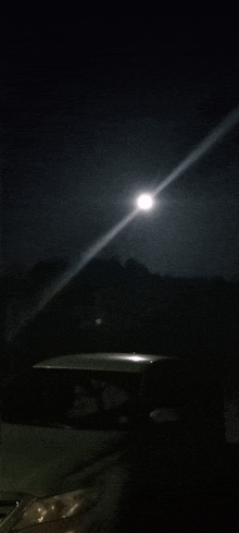 a car is parked in the dark with a full moon in the background