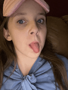 a young girl wearing a pink hat and a blue shirt sticking her tongue out