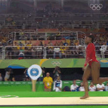 a woman in a red leotard is doing a routine in front of a crowd that is watching the olympics