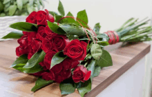 a bouquet of red roses with green leaves is sitting on a wooden table .