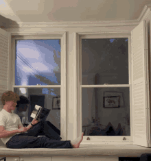 a man sits on a window sill reading a magazine