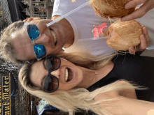 a man and a woman are holding coconuts with straws in front of a sign that says ' hawaiian market '