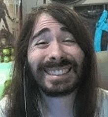 a man with long hair and a beard is smiling for the camera .