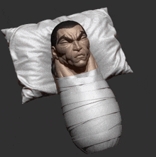 a statue of a man laying on a pillow wrapped in bandages