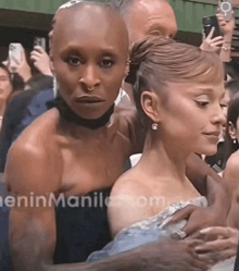 two women are standing next to each other in a crowd and one of them has a ring on her finger .