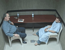 a man and a man in a hospital gown are sitting at a table talking to each other