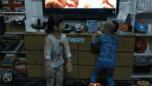 a little girl and a little boy are standing in front of a tv with the word happy on the dresser