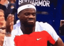 a man wearing a headband and a red shirt is giving a fist bump in front of a crowd .