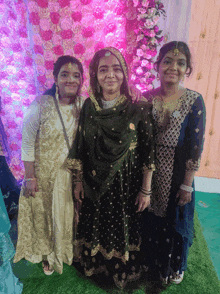 three women are posing for a picture in front of a pink flower wall