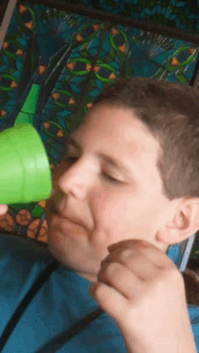 a boy in a blue shirt is holding a green cup in front of his face