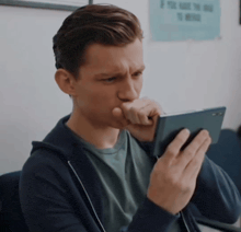 a man in a hoodie is looking at a cell phone in front of a sign that says if you have the time to read