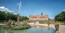 a large castle with a fountain in front of it and a pond surrounded by trees .