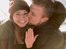 a man is kissing a woman on the cheek while she shows off her ring