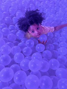 a young boy is playing in a ball pit filled with purple balls