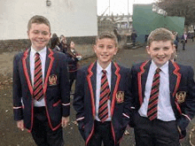 three young boys in school uniforms are standing next to each other .