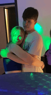 a boy and a girl are hugging in front of a green light