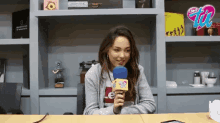 a woman sitting at a table with a microphone in front of a shelf with a sign that says club 100